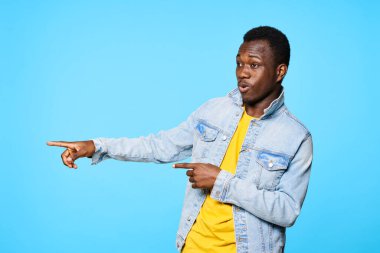 Genç Afrikalı bir adam mavi arka planda parmaklarını göstermiş.