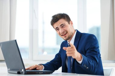 Genç yakışıklı iş adamı ofiste dizüstü bilgisayarla çalışıyor ve... 