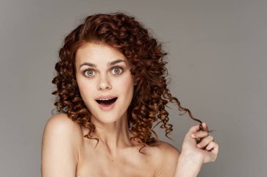 Kıvırcık saçlı, şaşırmış genç bir kadının portresi. Stüdyo çekimi