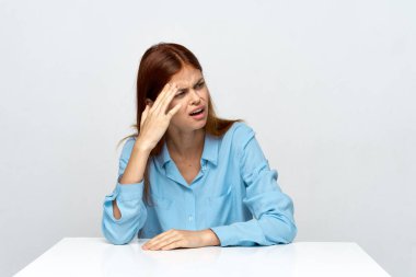 Stüdyo çekimi. Genç kızgın iş kadını masasında oturmuş başka tarafa bakıyor.