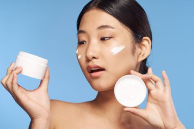 Stüdyo çekimi. Genç Asyalı kadın mavi üzerine krem sürüyor.