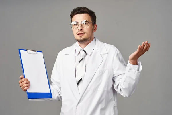 Studio shot. Young  confused doctor   with clipboard  isolated  on grey background