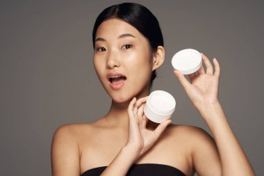 Stüdyo çekimi. Genç Asyalı kadın gride krem gösteriyor.