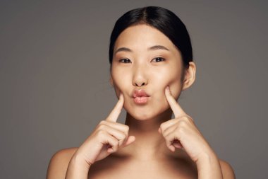 Young asian woman with fingers on cheeks 