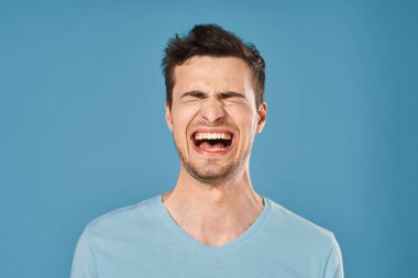 Stüdyoda mavi arka planda bağıran genç yakışıklı adam. 