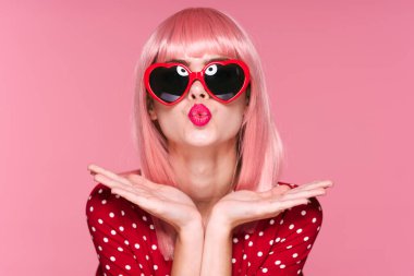 Pembe peruklu ve güneş gözlüklü genç bir kadın stüdyoda poz veriyor. 