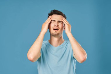 Stüdyoda mavi arka planda baş ağrısı çeken genç yakışıklı bir adam. 
