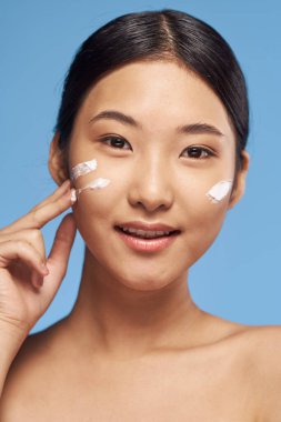 Genç Asyalı kadın yüzüne nemlendirici sürüyor. 