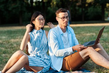 Dizüstü bilgisayarı olan genç öğrenciler çimlerin üzerinde oturuyor. 