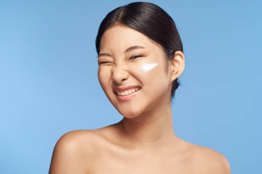 Genç Asyalı kadın yüzüne nemlendirici sürüyor. 