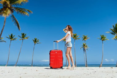  Kumsalda kırmızı valizli genç bir kadın.