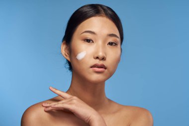 Genç Asyalı kadın yüzüne nemlendirici sürüyor. 