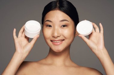 Stüdyo çekimi. Gri arka planda kremi olan genç Asyalı kadın.