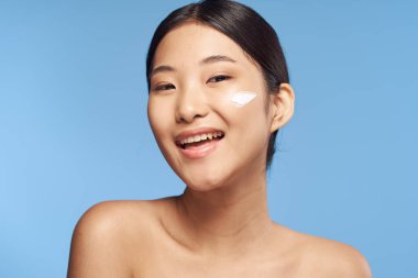 Genç Asyalı kadın yüzüne nemlendirici sürüyor. 