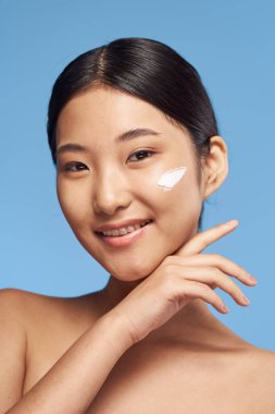 Genç Asyalı kadın yüzüne nemlendirici sürüyor. 