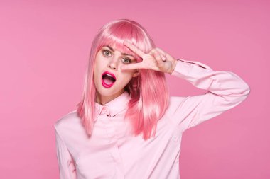 Pembe peruklu genç kadın pembe arka planda el kol hareketi yapıyor.