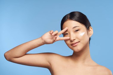 Genç Asyalı kadın stüdyoda mavi arka planda el kol hareketi yapıyor. 