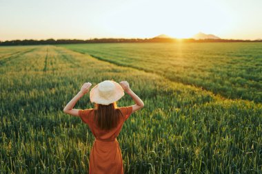 Gün batımında buğday tarlasında poz veren genç kadın.