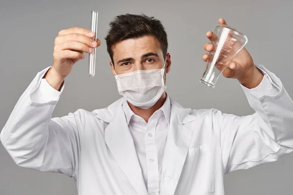 Young handsome doctor in mask  with empty  test tubes on grey background