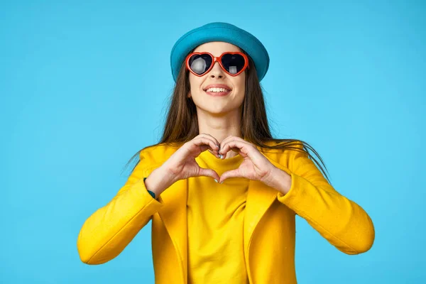 young beautiful woman in yellow jacket   showing heart  in Studio with blue Background.