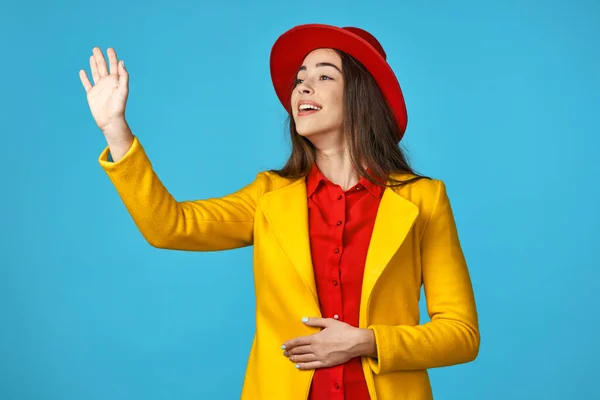 Young woman in yellow jacket   with hand up on  blue background.