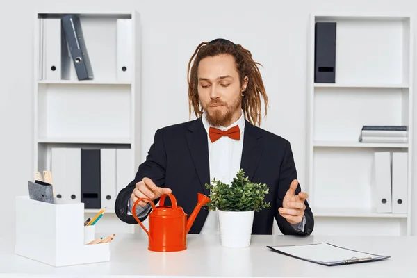 Young businessman sitting in the office with plant and watering can
