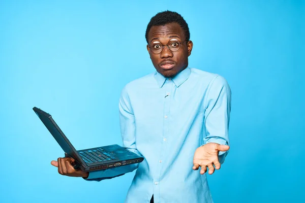 Young african surprised  businessman holding laptop isolated on blue background