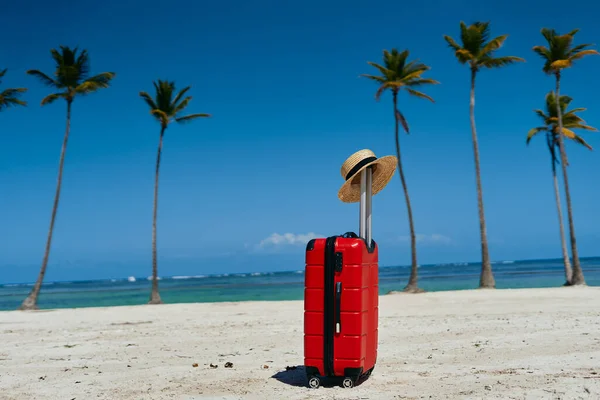 red suitcase and straw hat on th e beach