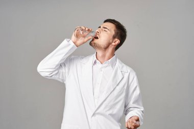 Laboratuvar önlüklü doktor gri arka planda test tüpünden su içiyor. Stüdyo çekimi