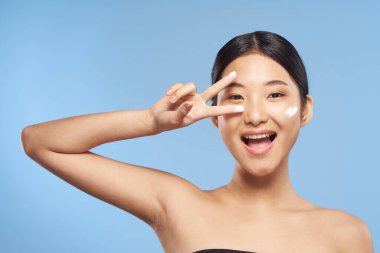 Genç Asyalı kadın yüzüne nemlendirici sürüyor. 