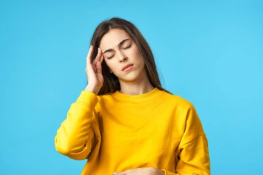 Stüdyoda başı ağrıyan genç bir kadın mavi arka planda izole edilmiş. 
