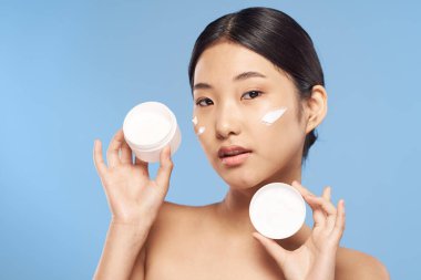 Stüdyo çekimi. Mavi arka planda krem gösteren genç Asyalı kadın.