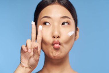 Genç Asyalı kadın yüzüne nemlendirici sürüyor. 