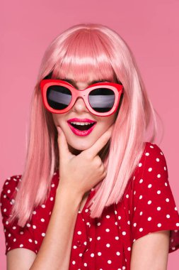 Pembe peruklu ve güneş gözlüklü genç bir kadın stüdyoda poz veriyor. 