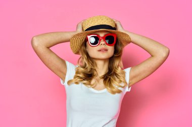 Stüdyoda pembe arka planda şapka ve güneş gözlüğü takan güzel bir kadın.      