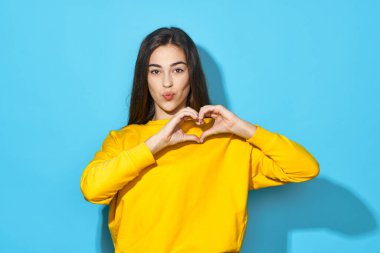 Stüdyoda kalp hareketi gösteren genç bir kadın mavi arka planda izole edilmiş. 