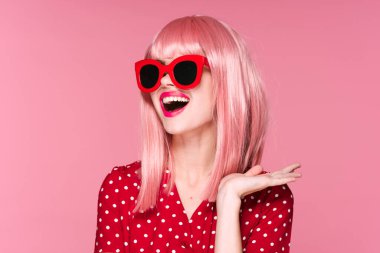 Pembe peruklu ve güneş gözlüklü genç bir kadın stüdyoda poz veriyor. 