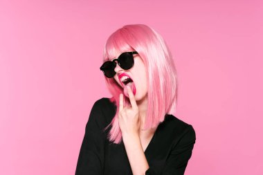 Pembe peruklu genç kadın pembe arka planda dilini gösteriyor.