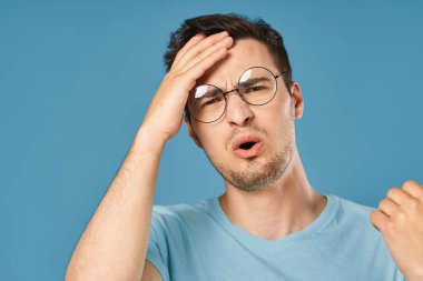 Stüdyoda mavi arka planda baş ağrısı çeken genç yakışıklı bir adam. 