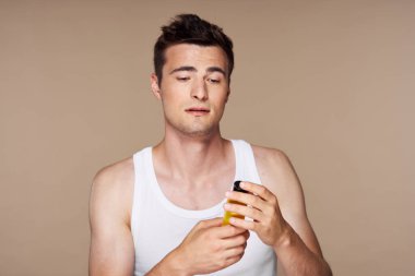 Stüdyo. Genç yakışıklı adam bej arka planda güzellik ürünleri tutuyor.