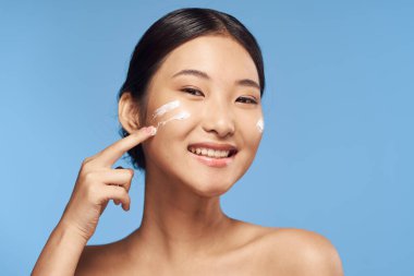 Genç Asyalı kadın yüzüne nemlendirici sürüyor. 