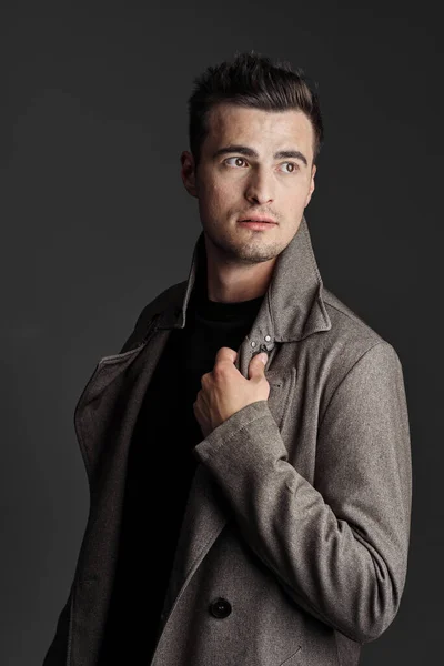 若い残酷な男ですコートで暗い灰色の背景にスタジオ — ストック写真