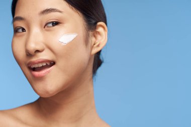 Stüdyoda mavi arka planda krem sürmüş genç Asyalı kadın. 