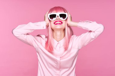 Pembe peruklu ve güneş gözlüklü genç bir kadın stüdyoda poz veriyor. 