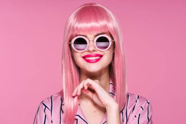 Pembe peruklu ve güneş gözlüklü genç bir kadın stüdyoda poz veriyor. 