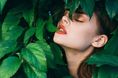 Yüzünde yapraklarla poz veren genç ve güzel bir kadın.