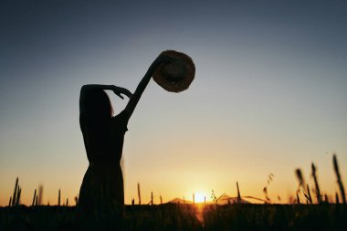 Gün batımında buğday tarlasında poz veren genç kadın.