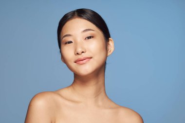 Stüdyo çekimi. Mavi arka planda poz veren genç Asyalı kadın.