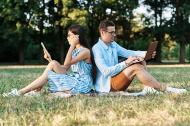Dizüstü bilgisayarı ve tableti olan genç öğrenciler çimlerin üzerinde oturuyorlar. 