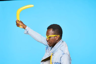 Bumeranglı genç Afrikalı adam mavi arka planda izole edilmiş.